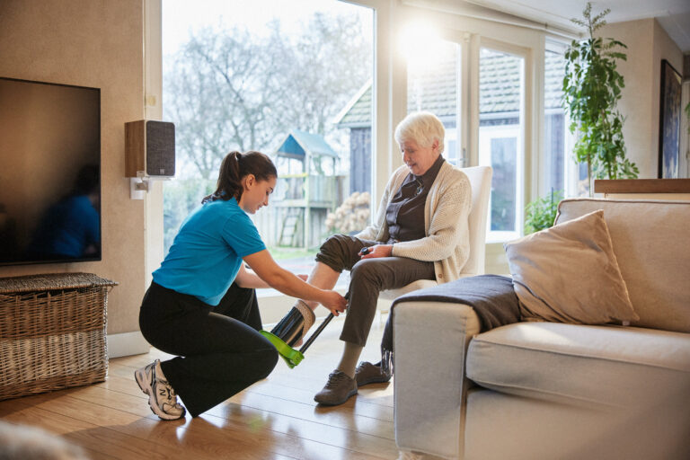 Thuiszorgmedewerker doet steunkous aan bij cliënt.